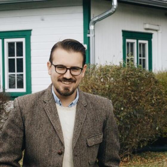 image of Jacob wearing a brown blazer and glasses smiling at the camera