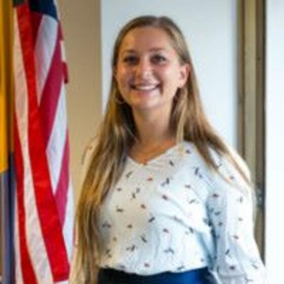 image of Kasey wearing a white blouse standing next to the American flag
