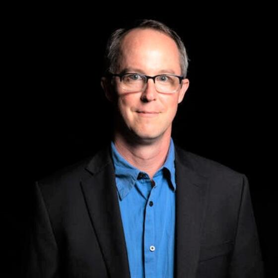 image of Douglas wearing glasses and a blue dress shirt smiling at the camera