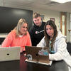 image of students sitting around desk looking at a laptop