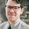 image of Sam Allingham wearing glasses in a grey shirt and black tie