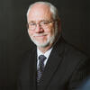 Kevin Delaney wearing a black suit and tie smiling and staring into the camera