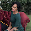 Tracey McPherson in a teal dress on a red couch smiling into the camera