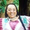 image of Brenda wearing a tie dye shirt standing in the woods smiling at the camera