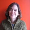 Christina Rosan in a gray sweater standing in front of a red background