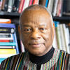 Molefi Kete Asante wearing a dashiki standing behind book and staring at the camera