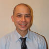 Ryan Omizo in a shirt and tie smiling and staring into the camera