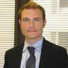 Adam Joseph Shellhorse in a black suit and tie staring into the camera