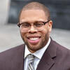 Timothy Welbeck wearing a gray suit with a tie smiling and staring into the camera