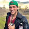 Thomas DiAgostino outside holding a drink in a green hat and black coat smiling and staring into the camera