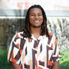 Trae Manzili in a white, brown and orange shirt smiling into the camera