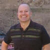 Michael Bognanno wearing a black shirt standing in front of a wall smiling and starting into the camera