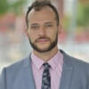 Bradley Gardener in a gray suit and tie with a pink shirt staring into the camera