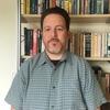 Hillel David Soifer in front of a book shelf staring into the camera