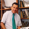 Murray Friedman in a teal tie standing in front of a book shelf staring into the camera