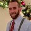Jesse Brey in a blue shirt with a red tie in front of some holiday decorations smiling into the camera