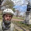 Jacob Shell outside in a bicycle helmet standing in front of a statue staring into the camera