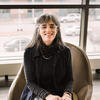 Laura Levitt sitting in a chair with a black shirt and colorful skirt on smiling and staring into the camera