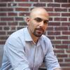 Mathieu Wimmer in a light blue shirt sitting in front of a brick wall staring into the camera