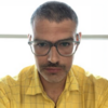 Max Andrucki in a yellow shirt and glasses staring into the camera