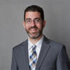 Michael Sances in a gray suit and tie smiling and staring into the camera