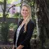 Nicole LePinewearing a black suit jacket and white shirt outside in front of a tree smiling into the camera