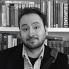 Philip Atkins standing in front of a book shelf smiling and staring into the camera