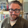 Robert Rabiee in a green shirt in front of a book shelf smiling into the camera